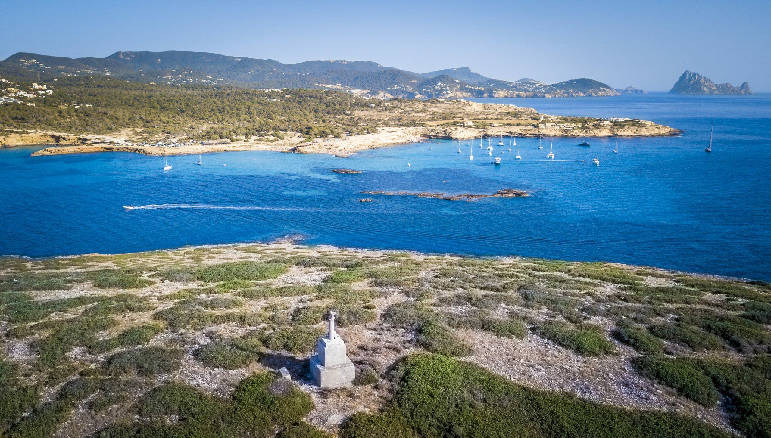 DJI_0043 Aerial view of Cala Comte, Ibiza, with turquoise waters, anchored sailboats and sandy coves along a rocky, pine-covered coastline.