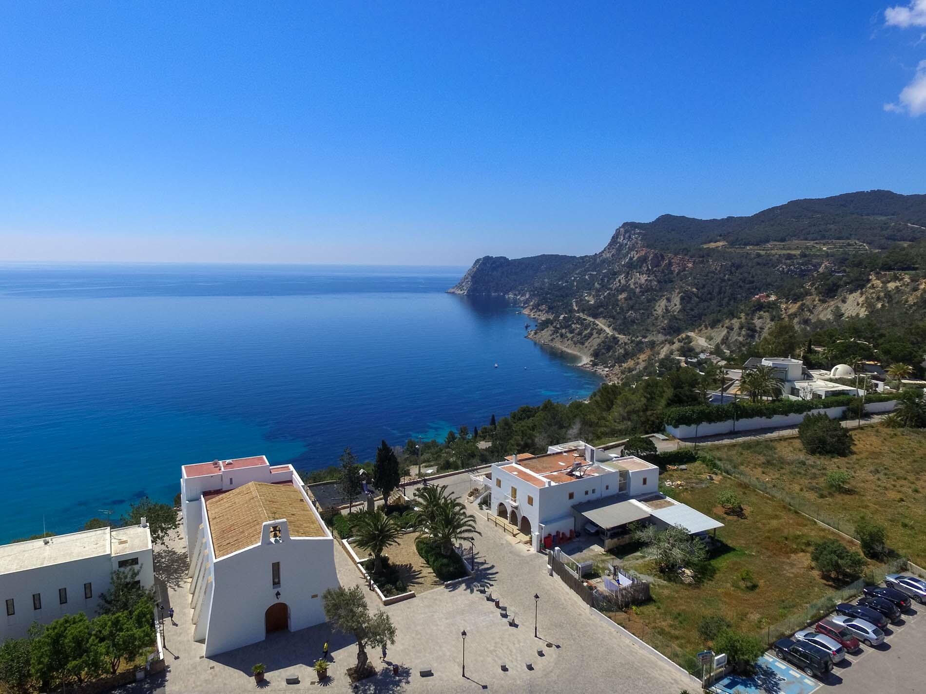 Elevated view of Es Cubells, Ibiza, with a whitewashed church overlooking the blue sea and rugged coastline